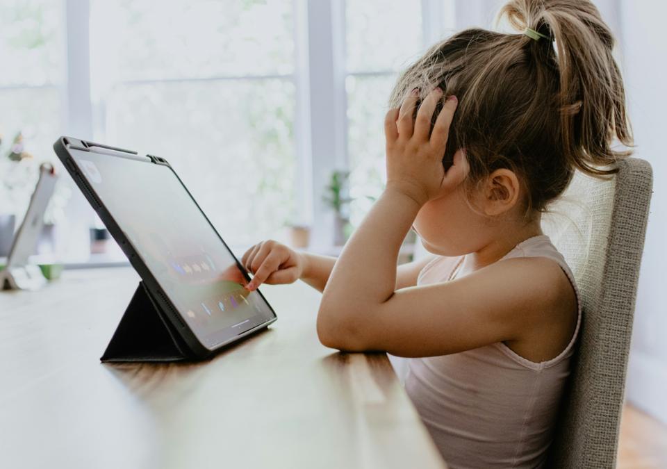 Nena petita asseguda davant d’una tauleta digital, representant l’ús de pantalles en la infància.